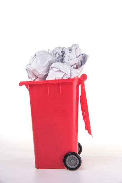 Verkrümmte Papiere in einem roten Müllkorb vor weißem Hintergrund