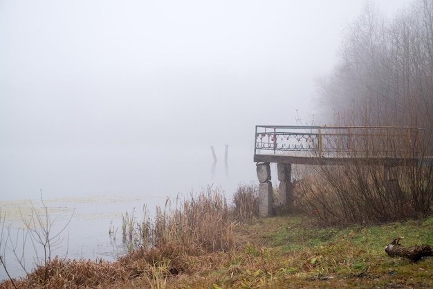 Verlassene verwitterte Pier am Seeufer bedeckt mit dünnem Nebel in der herbstlichen Landschaft des frühen Morgens