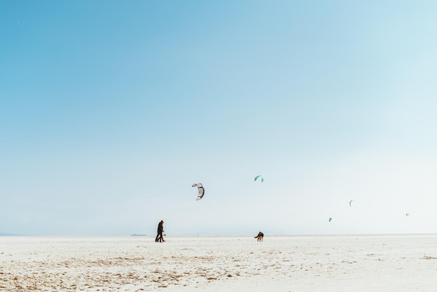 Verlassener Strandsand und nur in der Ferne ein fliegender Drachen und Punktfiguren von zwei Personen