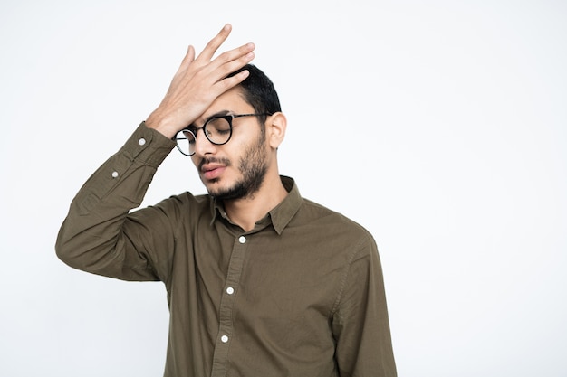 Verlegener Geschäftsmann mit Brille, der seine Hand auf der Stirn hält, während er versucht, sich an etwas zu erinnern