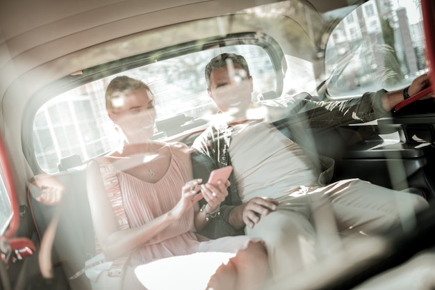 Verlegung der Strecke. Fröhlicher Ehemann und Ehefrau sitzen zusammen auf dem Rücksitz des Autos und schauen auf das Smartphone.