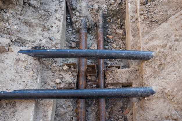 Verlegung von unterirdischen Regenwasserkanalrohren auf der Baustelle. Installation der Wasserleitung und des Abwasserkanals auf Turmdrehkränen im Hintergrund und blauem Himmel. Rohre des Grundwasserabflusssystems