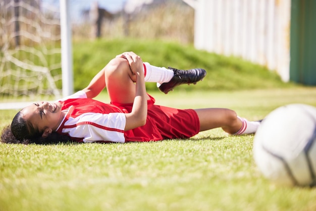 Verletzter Schmerz oder Verletzung einer Fußballspielerin, die während eines Spiels auf einem Feld liegt und ihr Knie hält Verletzte Fußballerin mit einem schmerzhaften Bein auf dem Boden in Qualen, die einen schlechten Tag auf dem Platz hatten