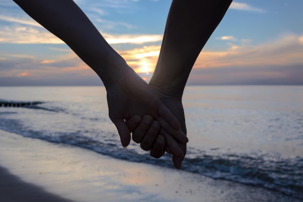 Verliebte Frau und Mann halten sich bei Sonnenuntergang an den Händen am Strand