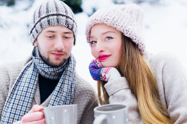 Verliebte Paare in warmen Kleidern sitzen eins nach dem anderen im Schnee und halten die Tassen in ihren Händen