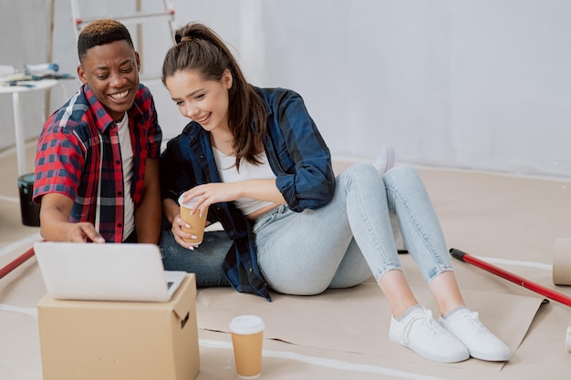 Verliebte Paare sitzen auf dem mit Kartons bedeckten Boden in einer renovierten Wohnung