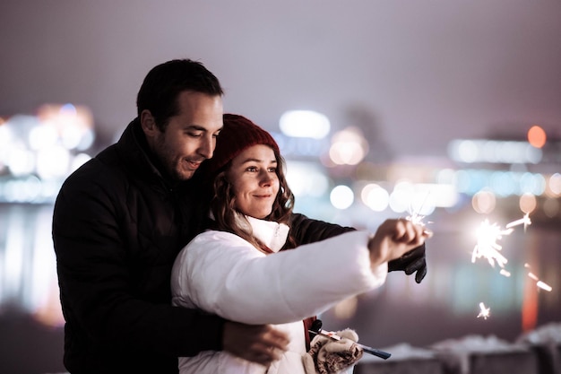 Verliebtes Paar bei einem Winterdate in der Stadt mit Wunderkerzen am Abend an den Weihnachtsfeiertagen.