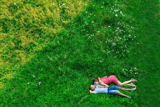 Verliebtes Paar, das am Sommertag auf der grünen Wiese liegt. Draufsicht von der Drohne