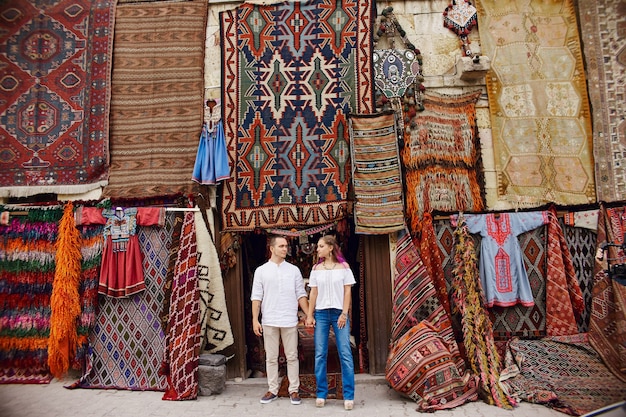 Verliebtes Paar kauft auf einem orientalischen Markt in der Türkei einen Teppich und handgemachte Textilien. Umarmungen und fröhliche Gesichter von Männern und Frauen