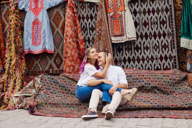 Verliebtes Paar kauft auf einem orientalischen Markt in der Türkei einen Teppich und handgemachte Textilien. Umarmungen und fröhliche Gesichter von Männern und Frauen