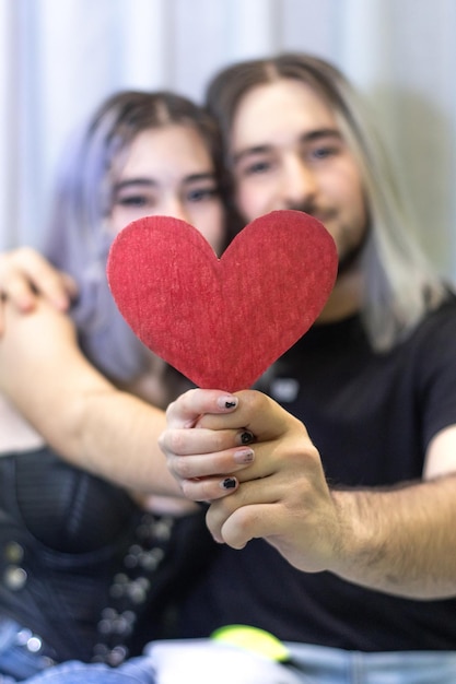 Verliebtes Paar sitzt auf dem Sofa mit einem Herz aus Papier Junges Paar in Liebe sitzt auf dem Sofa mit einem Herz aus Pappe