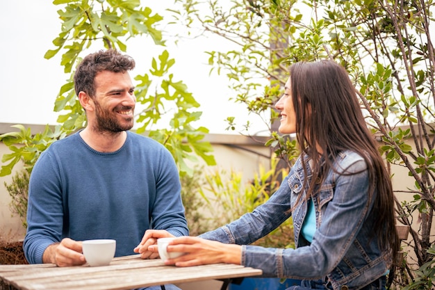 Verliebtes Paar trinkt heißes Getränk im Freien auf einer Terrasse, glückliches Paar spricht und flirtet, sitzt auf einem Tisch eines Cafés mit einer Tasse Kaffee oder Tee, Freizeit- und Relax-Lifestyle-Konzept