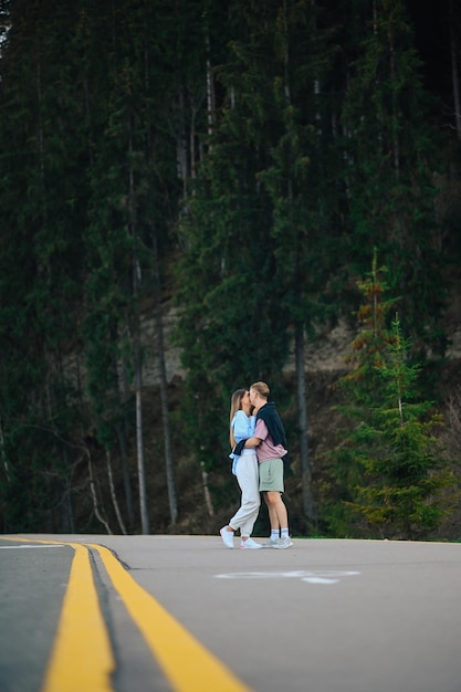 Verliebtes Paar umarmt sich im Wald und steht auf der Straße auf einem Hintergrund von Nadelbäumen