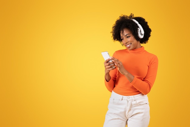 Verlobte junge afroamerikanische Frau mit lockigem Haar benutzt ein Smartphone