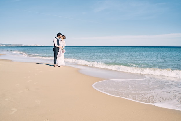 Foto verlobtes paar küsst am strand in brautkleidern