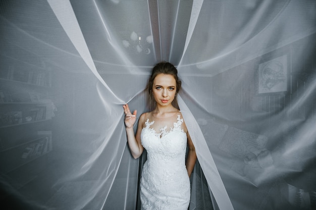 Verlockende junge Braut hebt ihre Hand, die unter dem weißen Vorhang steht