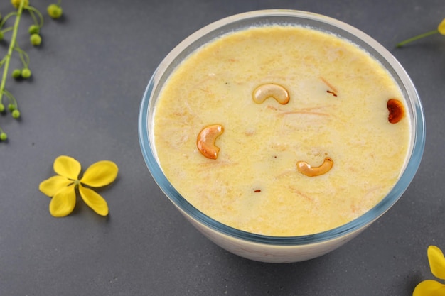 Vermecelli Payasam oder Kheer, südindisches Hauptsüßgericht aus Fadennudeln, Milch, Zucker und trockenen Nüssen, angeordnet mit Golden Shower Flower im grauen Hintergrund, selektiver Fokus.