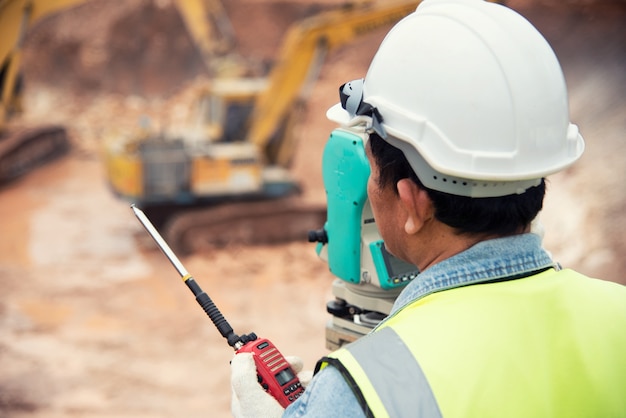 Vermessungsingenieur in der Baustelle benutzt den Theodolit, der Aushubfundamentarbeit überprüft