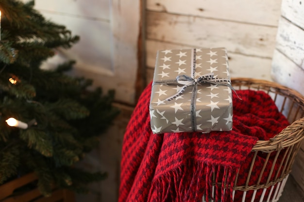 verpacktes Geschenk auf einer roten Decke in der Nähe eines Weihnachtsbaumes