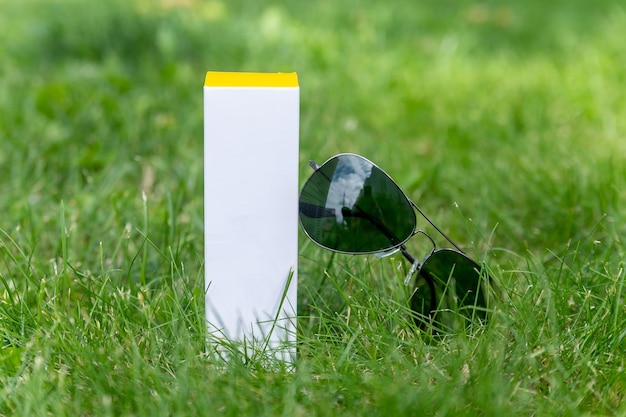 Verpackung aus einer Cremetube auf dem grünen saftigen Gras neben Sonnenbrille, Frische und Jugend