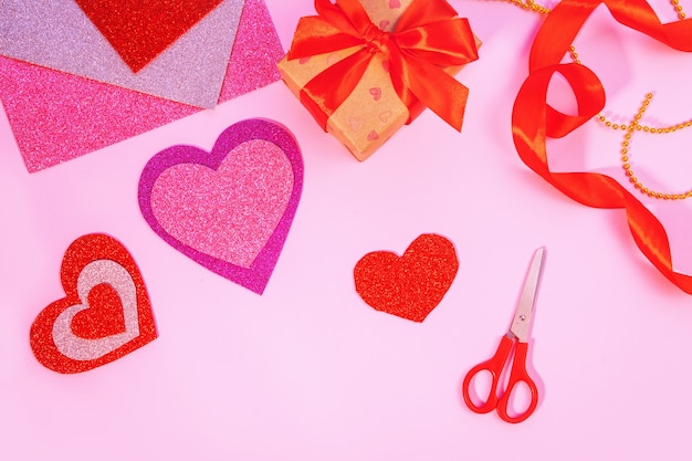 Verpackung Valentinstag oder Geburtstagsgeschenke. Valentinstaggeschenke mit einem roten Papierherz auf einer rosa Oberfläche. Draufsicht. Werkzeuge für handwerkliche Papierherzen.