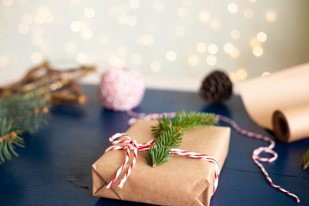 Verpackung von Weihnachtsgeschenken in Bastelpapier im Öko-Stil und Naturmaterialien, Tannenzweige auf blauem Holzhintergrund.