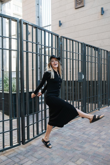 Verrückte blonde Frau mit schwarzen Kleidern, die an einem Zaun hängt