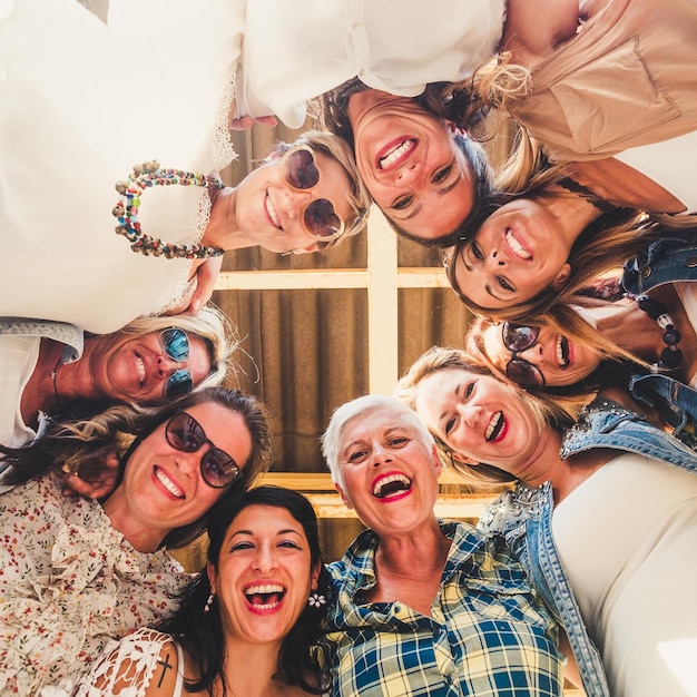 Verrückte Gruppe von Frauen in Freundschaft, die die Party auf der Terrasse genießen. Großes Lächeln, das auf die Kamera herabblickt. Komplizenschaft und Glück zusammen