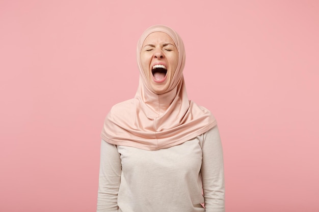 Verrückte junge arabische muslimische Frau in Hijab-leichter Kleidung posiert isoliert auf rosafarbenem Hintergrund Studioportrait. Menschen religiösen Islam Lifestyle-Konzept. Mock-up-Kopienbereich. Schreien mit geschlossenen Augen.