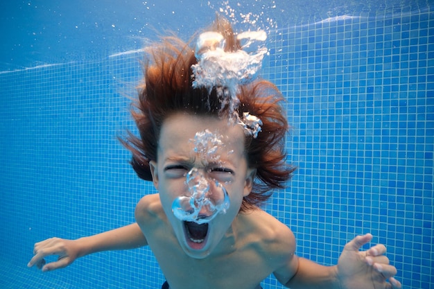 Verrückter Junge schreit mit geöffnetem Mund, während er im blauen Wasser des Pools schwimmt