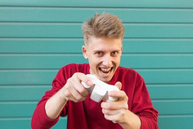 Verrückter junger Spieler in einem roten Sweatshirt und einem Joystick in der Hand, der Konsolenspiele spielt.