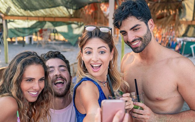 Versammlung junger Leute im Urlaub, die im Sommer ein Selfie unter einem Regenschirm am Strand lächeln