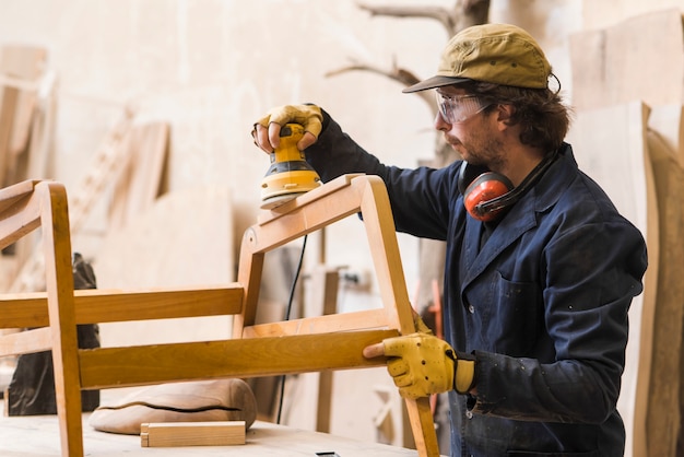 Foto versandendes holz des männlichen tischlers mit elektrischer sandpapierschleifmaschine