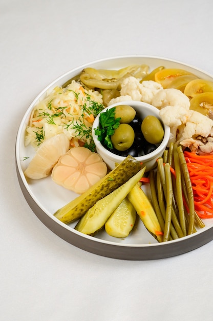 Verschiedene Arten von eingelegtem Gemüse auf weißem Hintergrund. Eingelegte Gurken, Tomatenkirschen, Gemüse, Pilze und Knoblauch mit Zwiebeln und Salat