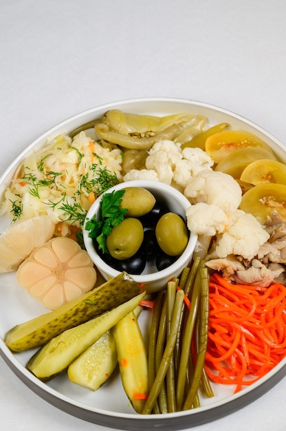 Foto verschiedene arten von eingelegtem gemüse auf weißem hintergrund. eingelegte gurken, tomatenkirschen, gemüse, pilze und knoblauch mit zwiebeln und salat