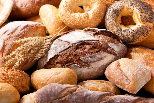 Verschiedene Arten von frischem Brot mit Weizenähren als Hintergrund