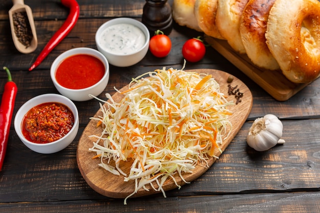 Foto verschiedene arten von saucen in schalen auf schneidebrett mit knoblauch und geriebenem kohl und tortillas. auf dunklem rustikal