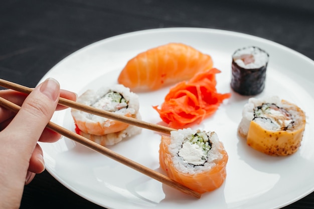 Verschiedene Arten von Sushi-Rollen auf weißen Platten auf schwarzem Hintergrund