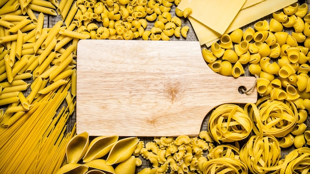 Verschiedene Arten von trockenen Nudeln und Spaghetti mit leerem Holzbrett
