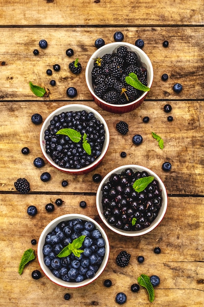 Verschiedene Beeren in blauen und schwarzen Farben: Heidelbeere, Blaubeere, Johannisbeere und Brombeere. Alter hölzerner Tischhintergrund, Nahaufnahme