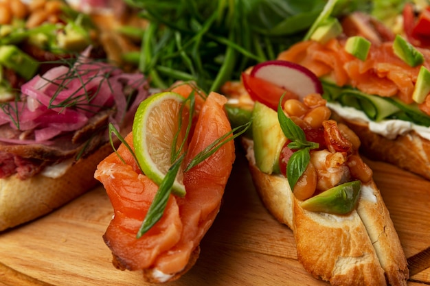 Verschiedene Bruschettas auf einem Holztablett. Fisch, Fleisch, Gemüse und Kräuter. Appetitliche Snacks. Nahaufnahme.