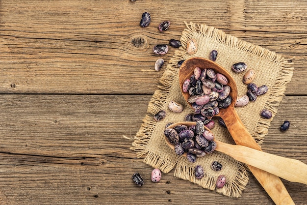 Verschiedene bunte Bohnen in großen Holzlöffeln. Rohe gesunde Zutat zum Kochen nützlicher Lebensmittel. Alter Holztisch, Ansicht von oben