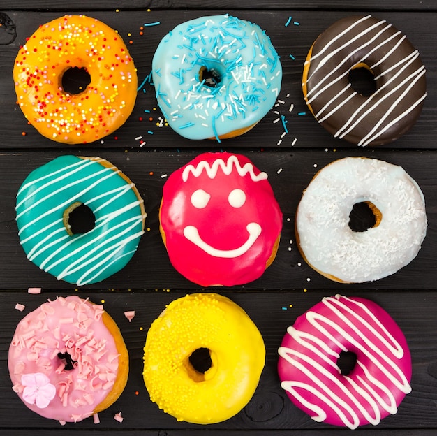 Verschiedene bunte Donuts auf schwarzem Holzhintergrund
