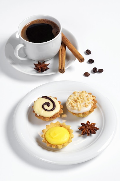 Verschiedene Cupcakes mit Zuckerguss in Teller Tasse Kaffee und Gewürz auf weißem Hintergrund