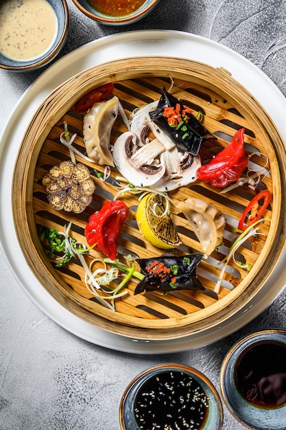 Verschiedene Dim-Sum-Vorspeisen in einem Bambusdampfer. Satz chinesisches Essen. Grauer Hintergrund. Draufsicht