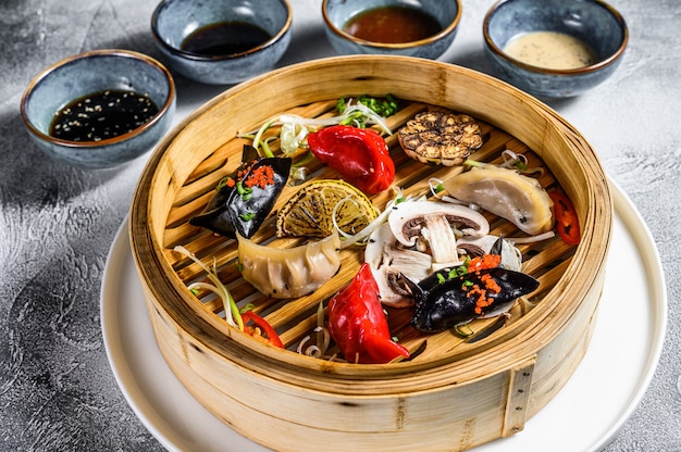 Verschiedene Dim-Sum-Vorspeisen in einem Bambusdampfer. Satz chinesisches Essen. Grauer Hintergrund. Draufsicht