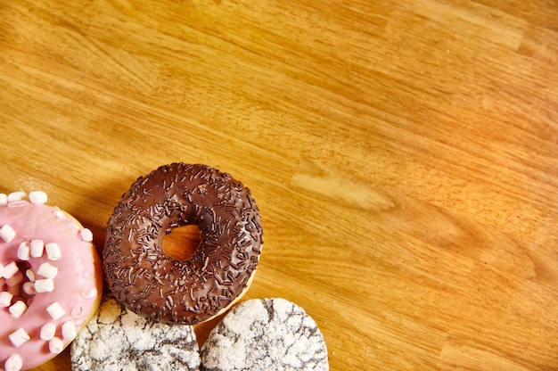 Verschiedene Donuts mit Streuseln auf Holzoberfläche. Hintergrund mit Kopierraum.