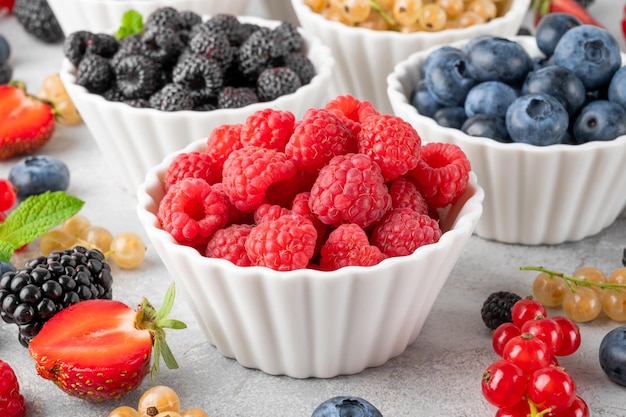 Verschiedene frische Beeren in Schalen auf grauem Betonhintergrund Konzept für gesunde Ernährung