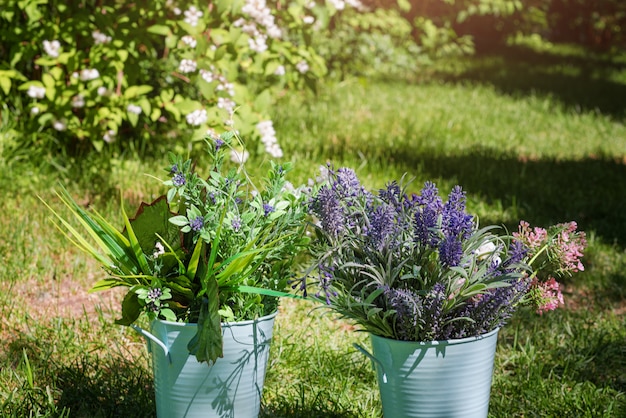 Verschiedene frische Blumenanordnung in Metalleimern im Garten. Dekorative Blumensträuße für festliche Anlässe.