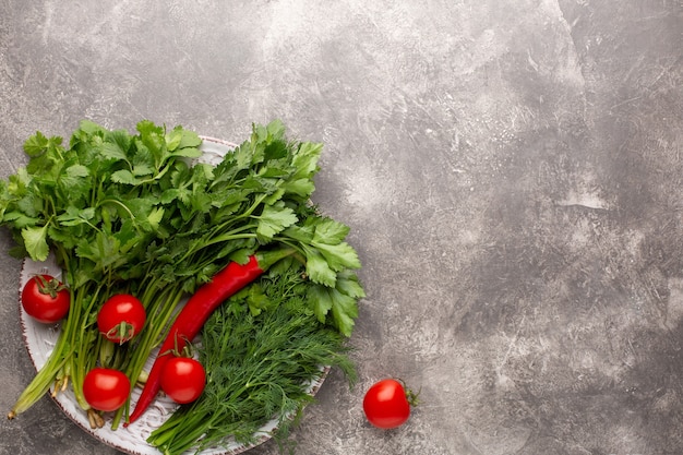 Verschiedene frische Grüns, Tomaten und Chili auf rundem Teller auf grauem Beton. Draufsicht.